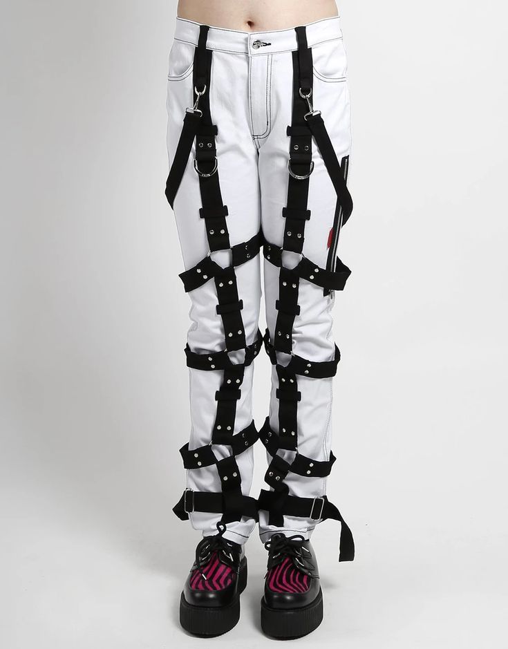 a person is wearing white denim pants with black straps around their legs. they are wearing black and pink boots and there is a white background.