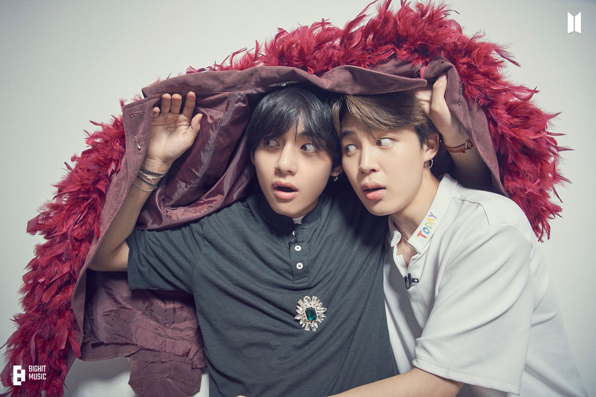 the image shows bts members v and jimin posing together. they are underneath a marooncolored jacket with red feathers around the collar. both have surprised expressions on their faces. v is wearing a dark gray shirt with a large decorative brooch, while jimin is in a white polo shirt with the word "today" embroidered on the collar. the bts and bighit music logos are visible in the upper right and lower left corners of the image, respectively.