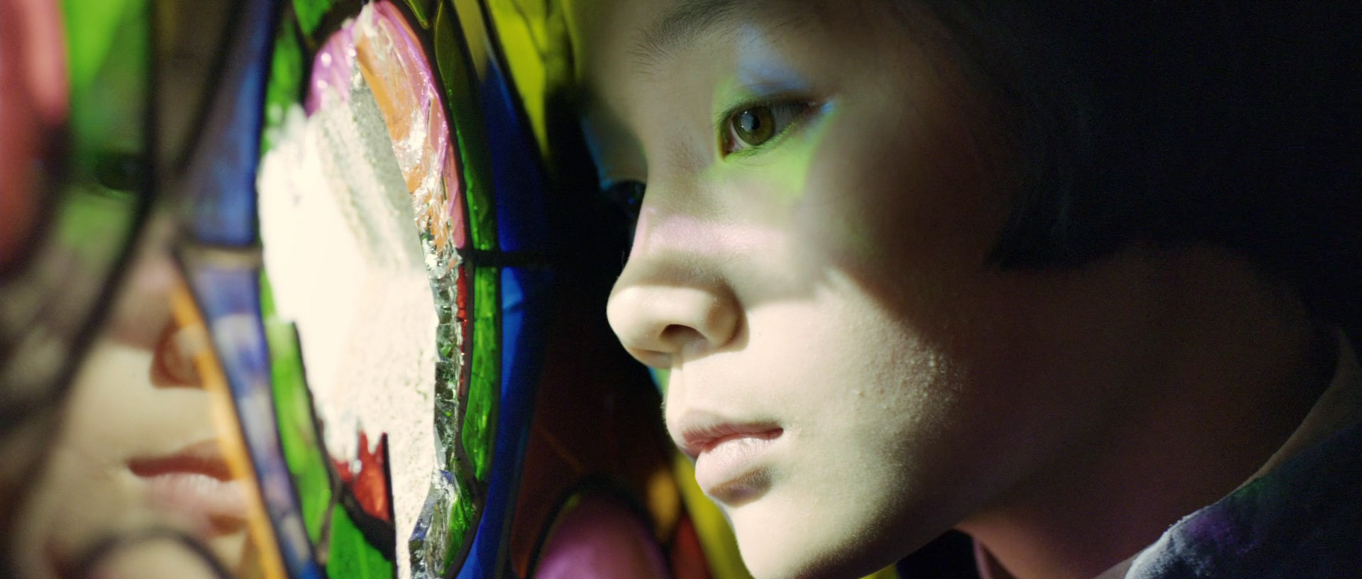 a closeup of a child's face as they look intently at something offcamera. colorful lights, likely from stained glass, are projected onto their face, highlighting their features and creating a sense of wonder.