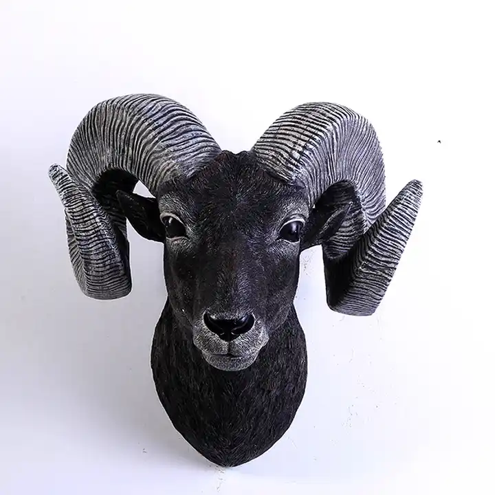 the image shows a closeup of a black and gray resin ram head sculpture.  the sculpture is highly detailed, showcasing realistic texturing on the ram's face and impressive, curled horns. the ram's expression is serene, and the overall color palette is dark and sophisticated. it appears to be designed as a wallmounted decorative piece for home decor, reminiscent of faux taxidermy.  the background is a plain white, emphasizing the sculpture.