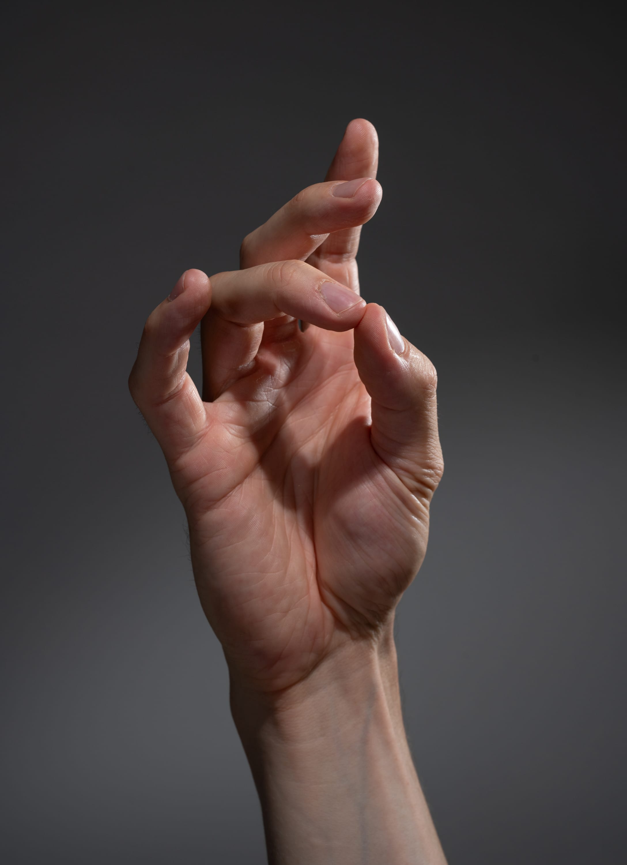 an adult's left hand is shown with the index and middle fingers touching the thumb. the background is a gradient gray. the image is lit with studio lighting.