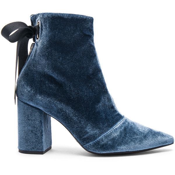 a single blue velvet ankle boot is shown in a studio shot against a white background. the boot has a thick block heel, pointed toe, and a black ribbon detail at the back. the velvet material is plush and reflects light, giving the boot a luxurious appearance.