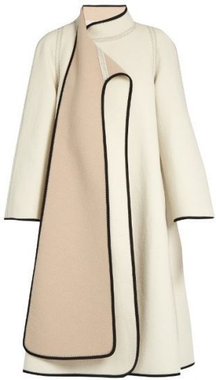 a stylish offwhite wool coat with beige paneling and black trim. the coat has an oversized fit, long sleeves, and a high neck.