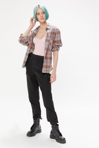 a fullbody studio shot of a female model showcasing an outfit from urban outfitters. she is wearing a grey and brown plaid flannel shirt over a pink bodysuit, black cargo pants cuffed at the ankles, and black doc martens combat boots. her hair is styled in a short, teal bob. the background is plain white.
