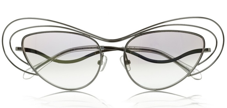 a pair of erdem designer sunglasses is displayed against a white background. the sunglasses have a unique, abstract design with silver wire frames and gradient lenses, fading from darker at the top to lighter at the bottom. the frames feature additional looping wire elements that extend above and around the lenses.