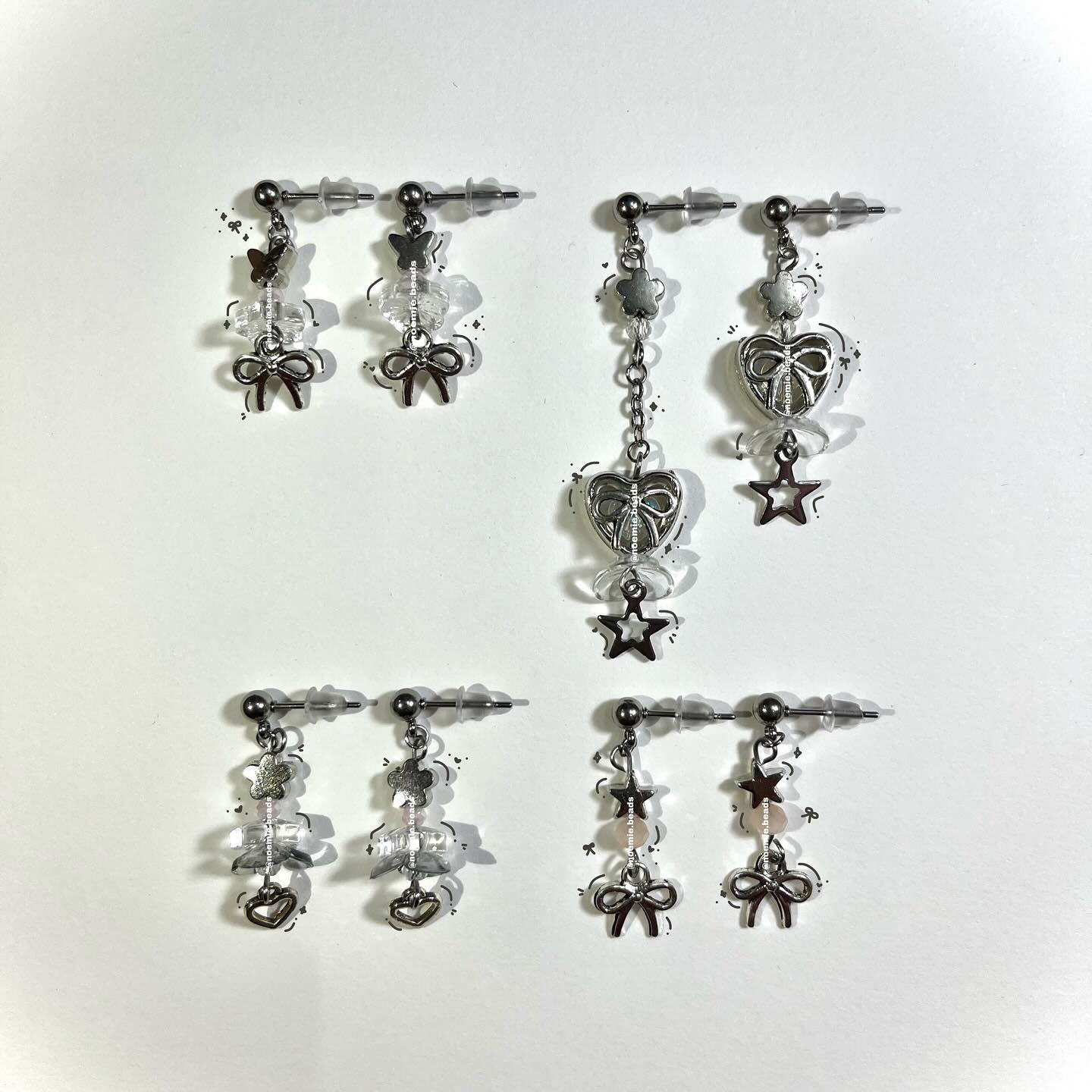 a collection of silver earrings featuring different designs with bows, stars, hearts, and beads, laid out on a white surface.