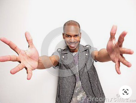 a man wearing a grey vest over a camouflage shirt stands against a white background. he is smiling and extending his arms toward the camera with his hands open, as if in welcome. the photo is taken with a fisheye lens.