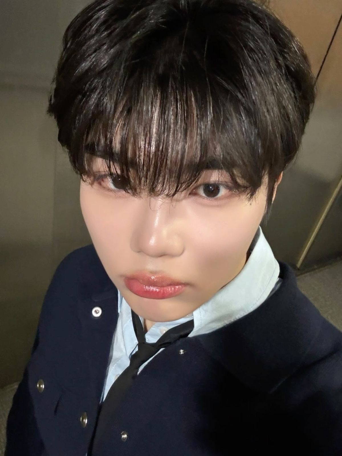 this is an eyelevel, closeup selfie of a young asian man with short black hair wearing a navy blue collared shirt under a navy blue jacket.  he is wearing a black skinny tie. the photo appears to be taken indoors under artificial lighting. the man has a neutral expression on his face.  the photo is slightly blurry.