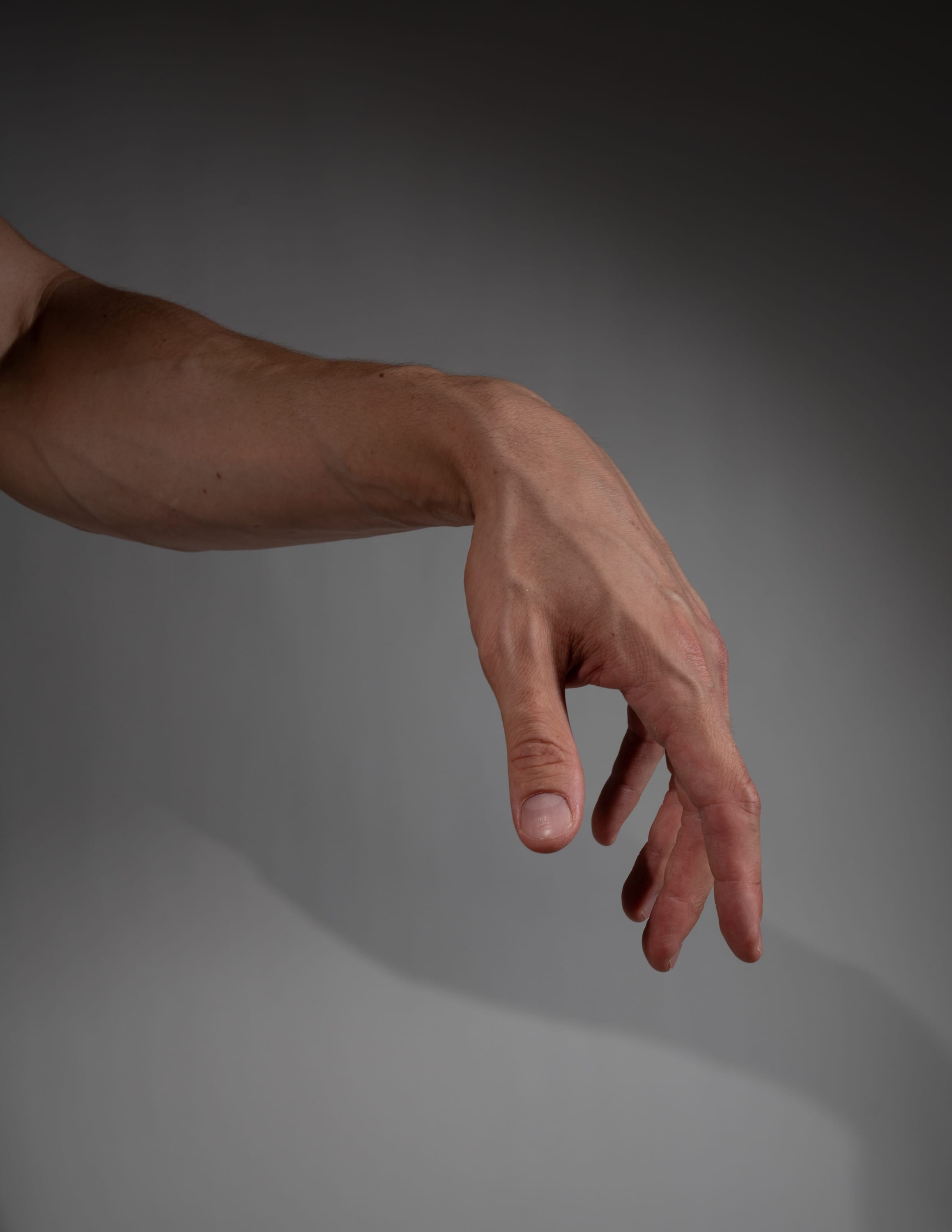a closeup image of a fair skinned male's right arm and hand extended down with the hand open and relaxed.  the background is solid gray and the lighting is soft.