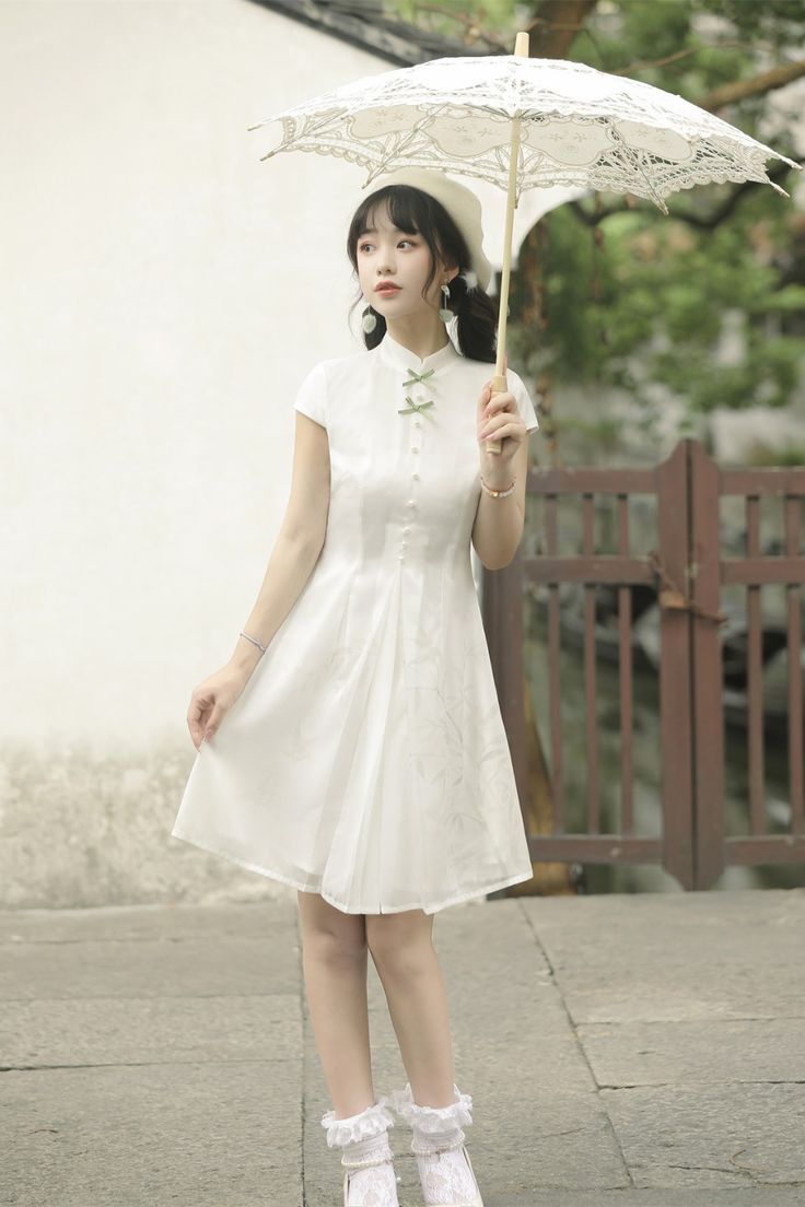 a young woman in a white chinesestyle dress stands on a paved path. she holds a white lace parasol over her head and smiles gently at the camera. the dress features short sleeves, a mandarin collar, and a flowy skirt. the woman is also wearing a white beret, white socks, and white shoes. the background showcases a traditional chinese building with a wooden fence and gate. lush greenery peeks through the architectural elements, creating a serene and elegant atmosphere. the scene is bathed in soft, natural sunlight.