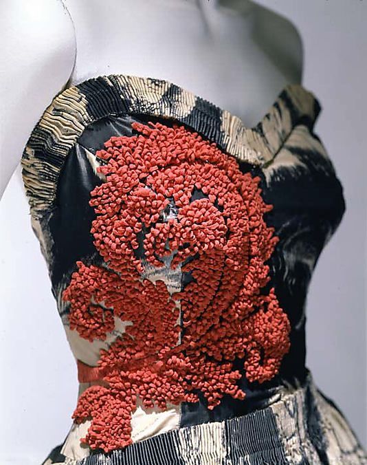 a closeup shot showcases a strapless dress featuring intricate red embroidery on the bodice. the dress is made from a patterned fabric in black, white, and beige hues. the overall aesthetic suggests a highfashion, couture piece.