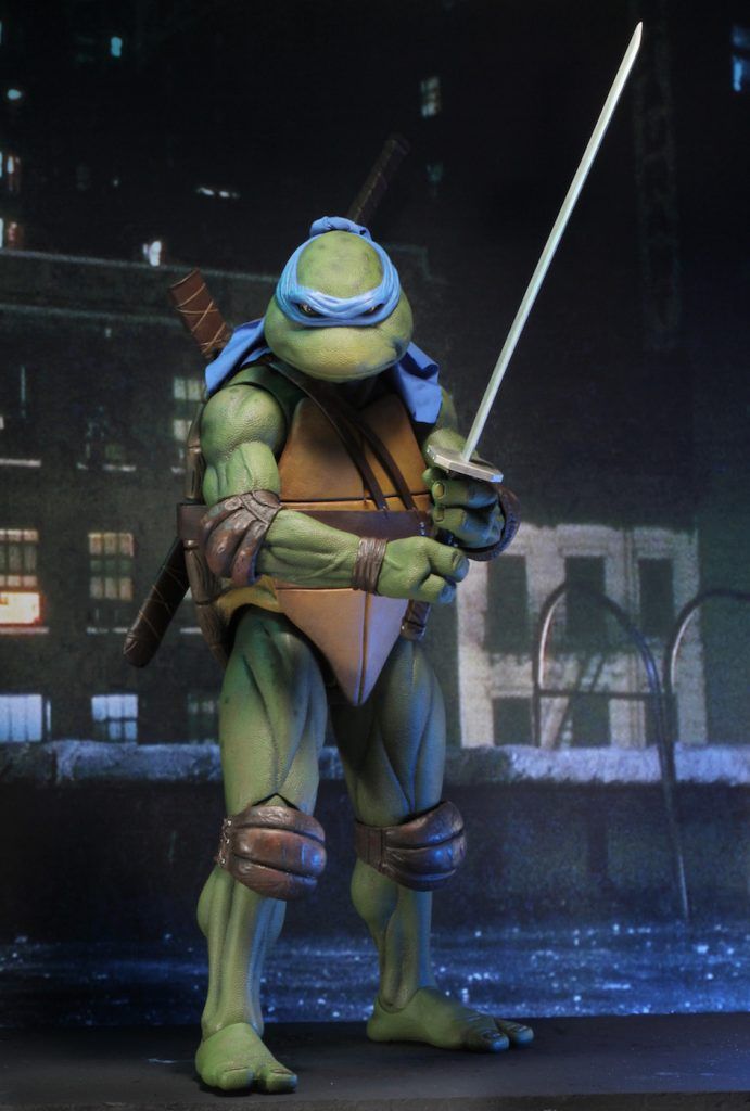 a closeup shot of the leonardo action figure from the teenage mutant ninja turtles. leonardo stands in a fighting stance, holding his katana sword in his right hand. he wears his signature blue mask and is standing in front of a cityscape. he is posed as if he is about to strike.