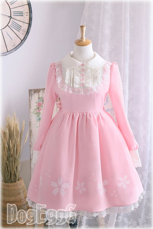 a pink lolita fashion dress with white lace collar and cuffs is displayed on a mannequin. the dress has a floral print on the skirt and is made of a soft, flowing fabric. the background is a white wall with a clock and a window.
