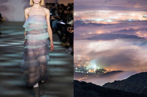 a fashion model in a sheer, layered dress walks the runway during a fashion show. the background is a cityscape with lights, but the city is mostly obscured by fog and clouds. the model's dress is similar in color to the fog and clouds, creating a harmonious effect. the model's pose and the overall aesthetic are elegant and ethereal. the image creates a sense of mystery and intrigue.