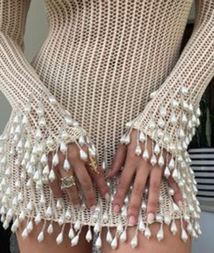 a woman wearing a white beaded dress with pearls. she is posing for a photo and her hands are resting on the front of the dress.
