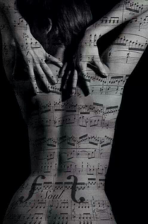 the image is a striking monochrome photograph of a woman's back. her body is overlaid with a sheet of musical notation, creating a visually arresting effect.  the music appears to be integrated directly onto her skin, almost as a tattoo or body paint. the woman's hands rest gently on her back, framing the musical score. the overall mood is sensual, artistic, and mysterious, with the use of shadow and stark contrast enhancing the image's dramatic quality. the word "soul" is visible within the musical notation printed on her back.