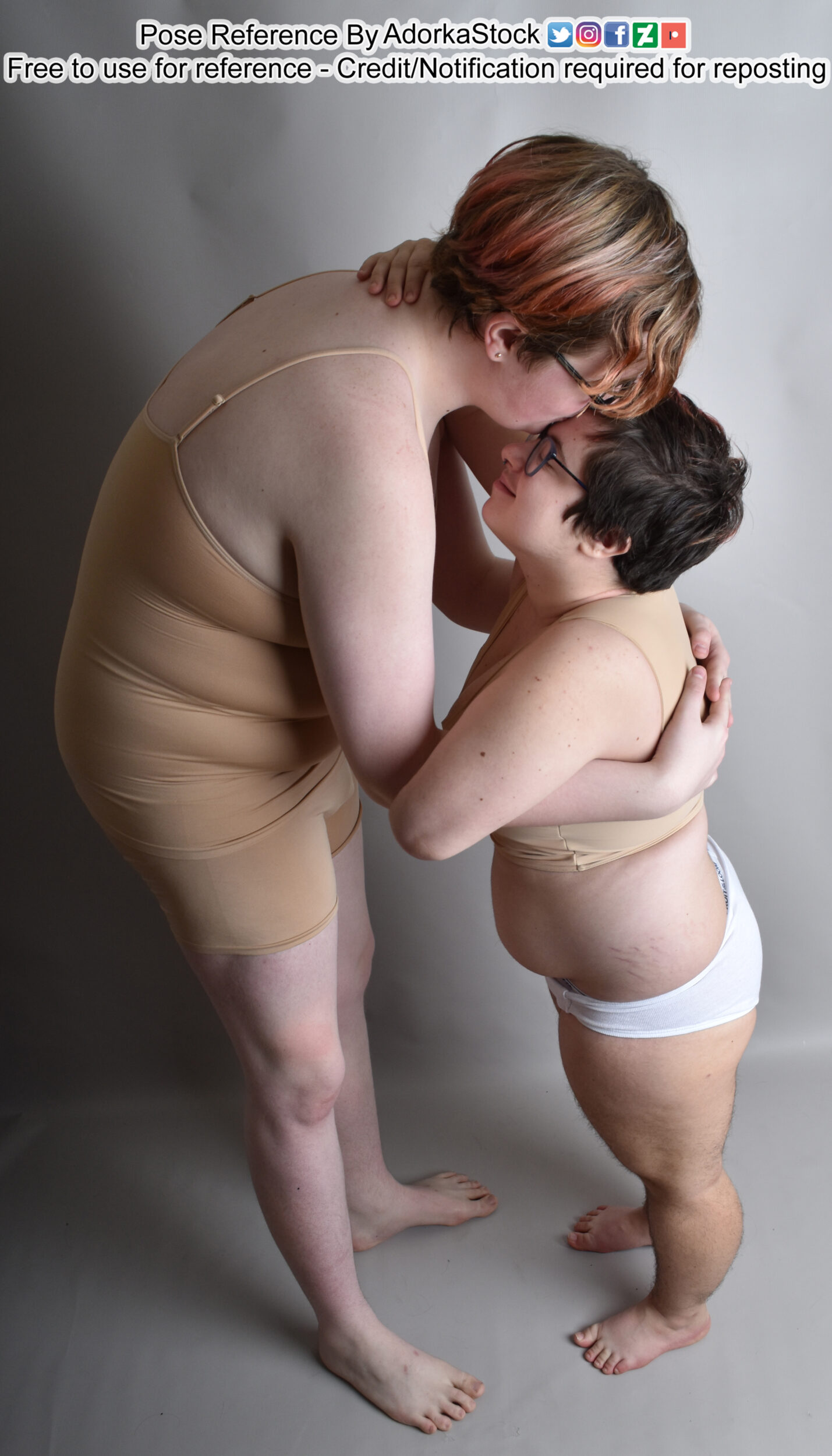 two women are hugging in a loving embrace. the woman in the front is taller and is hugging the woman in the back. the woman in the back is shorter and is hugging the woman in the front. they are both wearing white underwear. they are standing on a grey background.