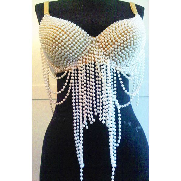 a pearl bra top on a black mannequin. the bra is made of densely packed white pearls and has straps made of tan material. strands of white pearls hang down from the bra, creating a fringe effect. the background is simple and slightly out of focus.