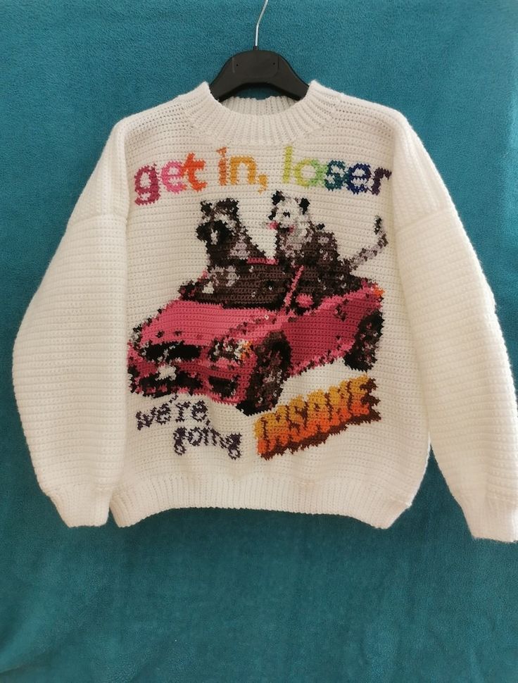 a white sweater with a black hanger in the background. the sweater has the words "get in, loser" on top in colorful sequins. below that are two animals in a pink car made out of sequins. the bottom has the words "we're going insane" in sparkly orange sequins.