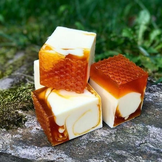 a closeup shot of three handcrafted honey soap bars.  the soaps are stacked on top of each other and are made with natural ingredients, like beeswax. the soap bars are a beautiful white and yellow color, and the texture is rich and creamy. this is a perfect image to use for a product page for homemade honey soap bars.