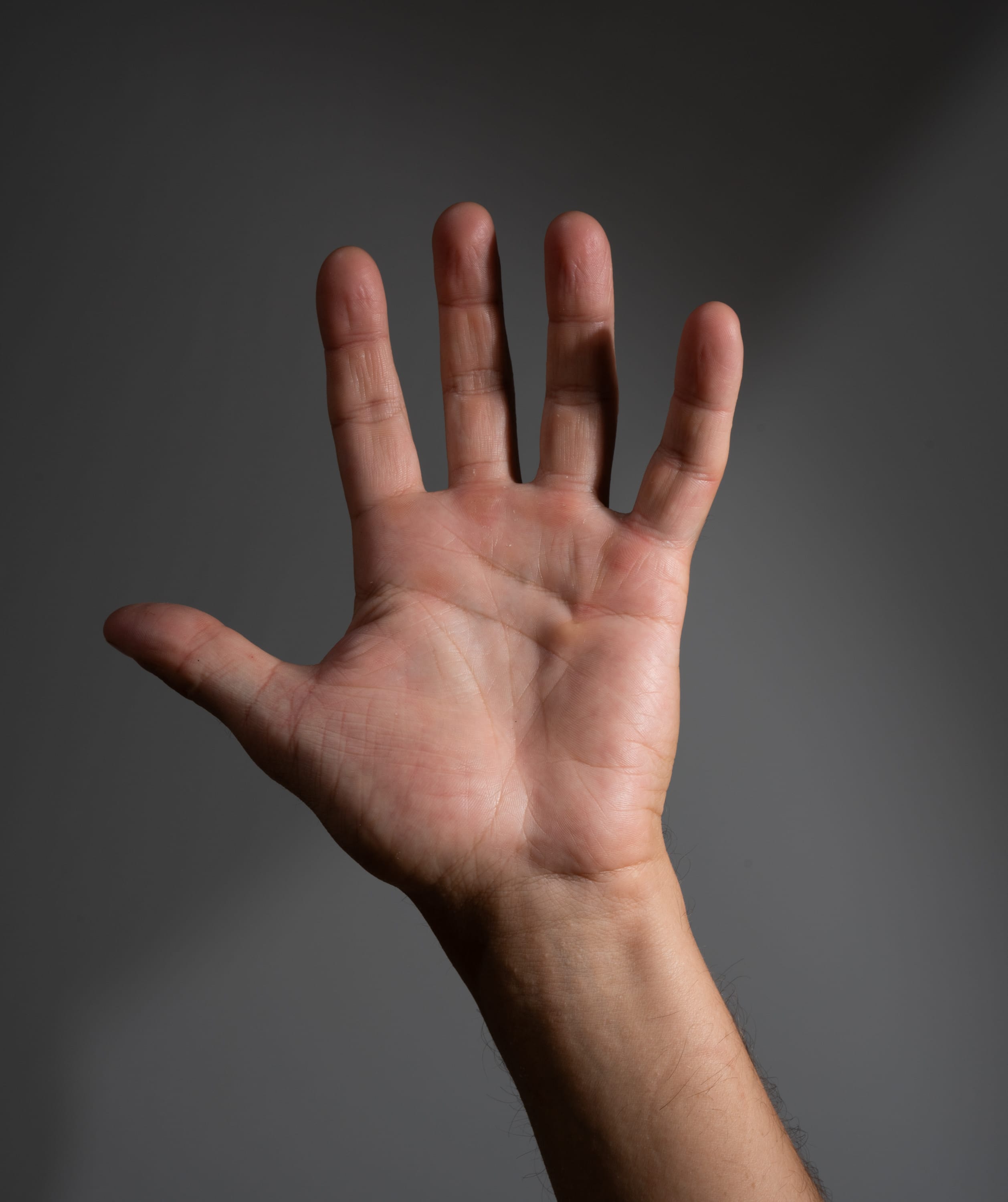 a closeup view of a male hand extended with fingers spread, illuminated by studio lighting against a dark gray backdrop. the image highlights the details of the skin and the subtle shadows cast by the lighting.