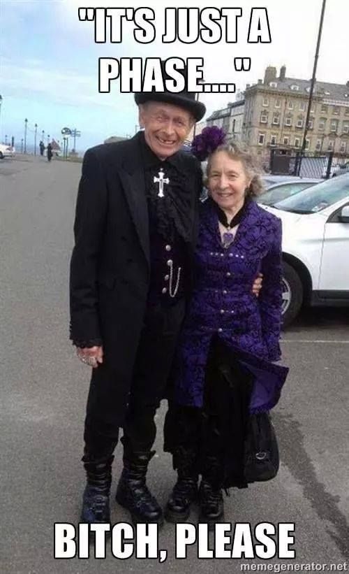 an elderly couple dressed in goth attire stands in a parking lot. the image has the caption "it's just a phase...." above them and "bitch, please" below them, suggesting the image is used as a meme related to longterm commitment to a subculture.