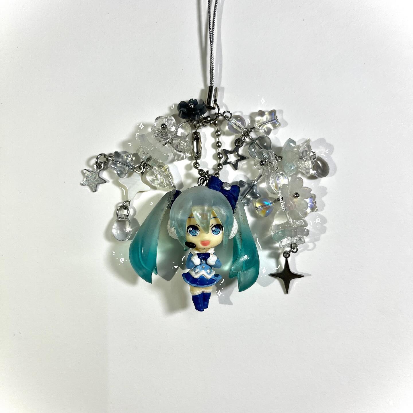 a hatune miku figurine keychain with clear beads, star and flower charms against a white background.