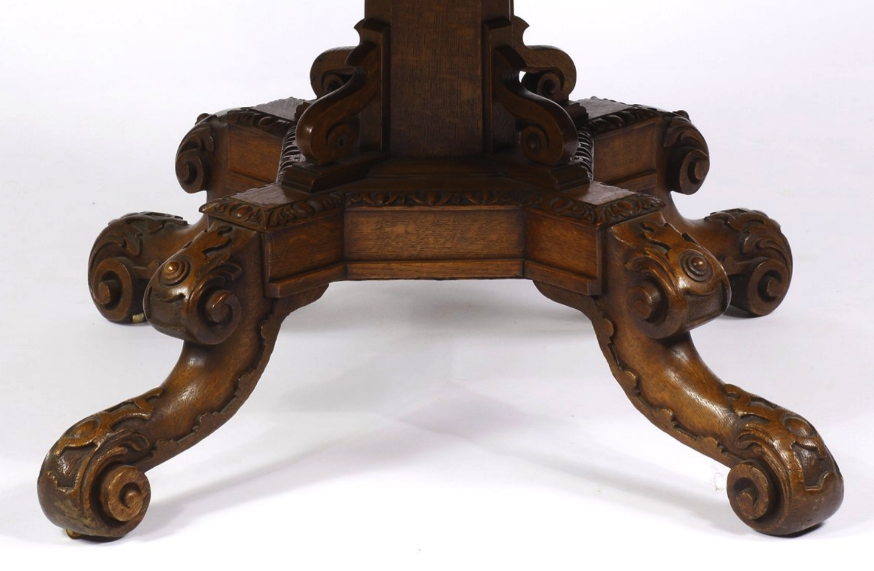 closeup of the elaborately carved, wooden base of a table. it has four legs that each end in a claw foot. the base is decorated with intricate scrollwork and floral motifs. the table is an antique piece with exquisite craftsmanship.