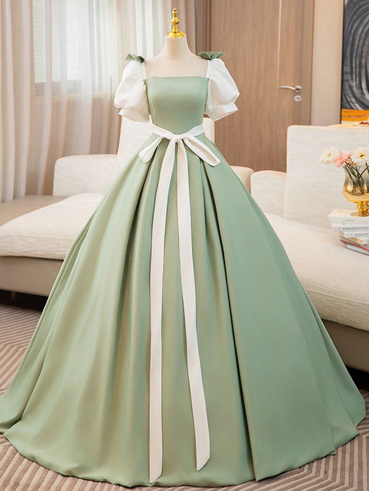 a green satin ball gown with puff sleeves and a square neck. the dress is tied with a white ribbon. the dress is displayed on a mannequin.