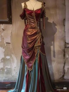 a mannequin is wearing a long, flowing dress with a vintage look. the dress is a deep red and teal color with gold accents. it has a sweetheart neckline and offtheshoulder sleeves. the dress is formfitting on top and flows out into a long, full skirt. the mannequin is positioned in front of a weathered wall, which adds to the vintage feel of the image.