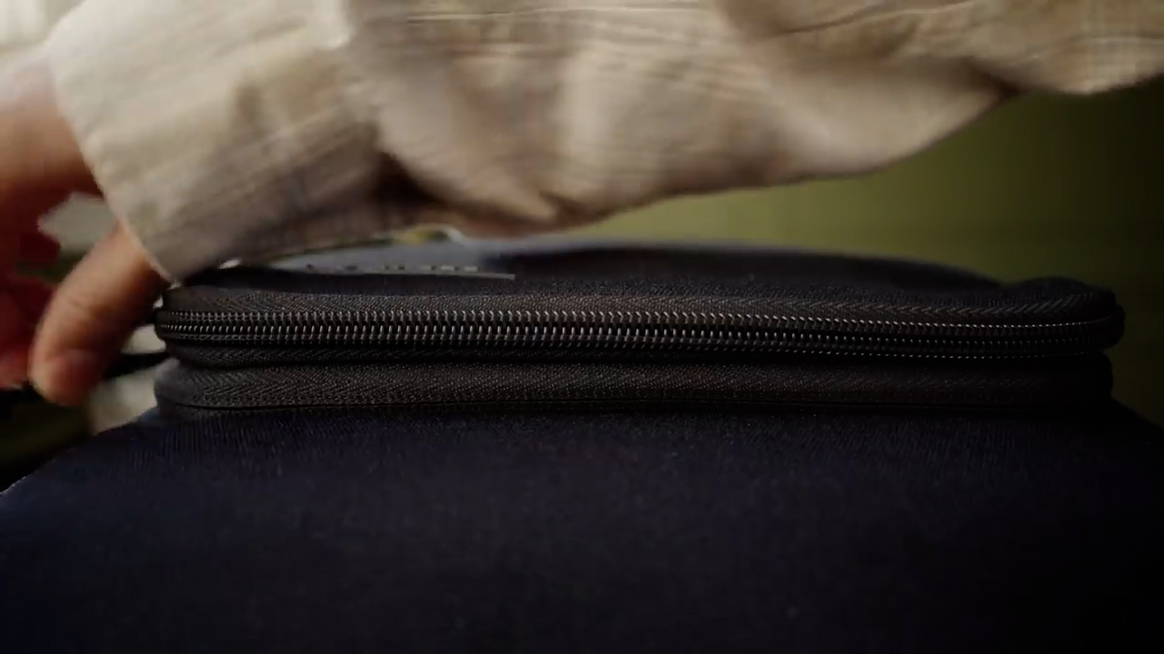 a closeup shot of a person's hand slowly opening the zipper of a black piece of luggage. the lighting suggests an indoor setting with soft, natural light.