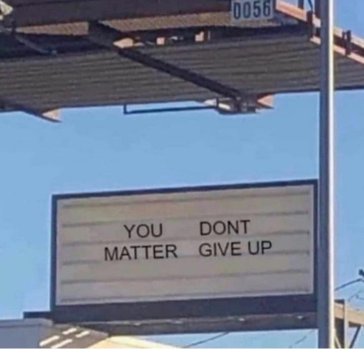 a white billboard with black lettering that reads "you matter don't give up" is mounted to a metal pole. the billboard is against a clear blue sky with clouds. it is likely located on a street in an urban area. the billboard is a positive and motivational message.