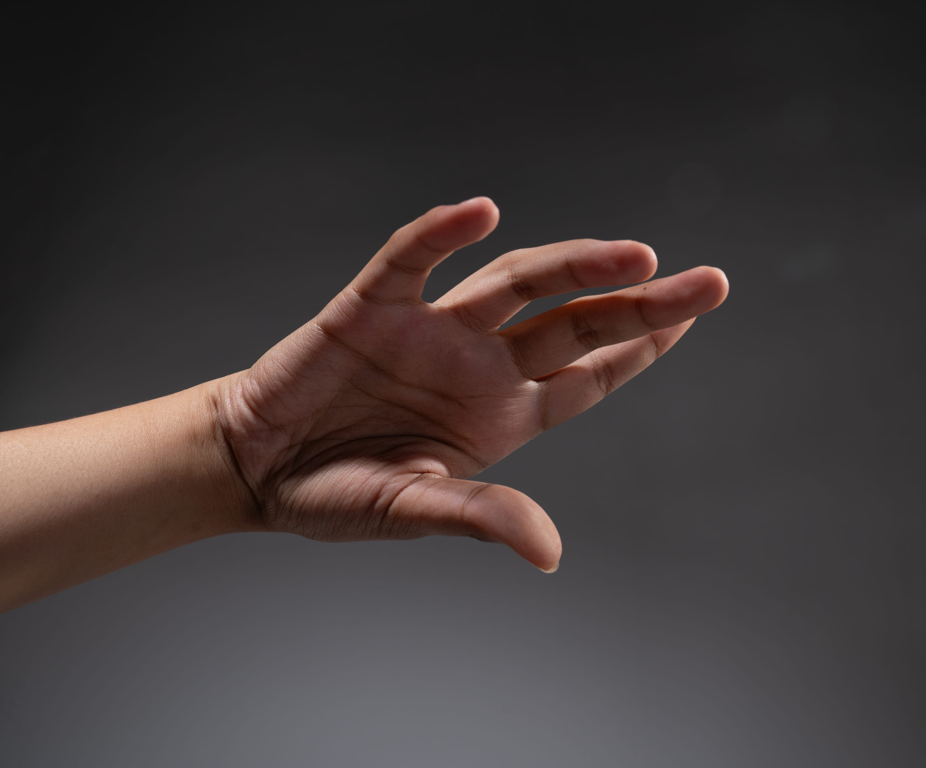 a left hand of a person is reaching forward against a gray background.