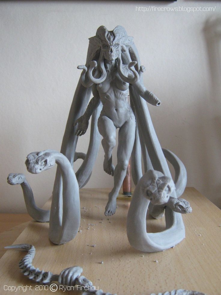 a gray clay sculpture of medusa stands on a wooden table. she is a fearsome figure with snakes for hair, and her body is posed in a dynamic, serpentine manner. the sculpture is very detailed, and the artist has captured the creature's terrifying beauty.  the lighting is bright and natural, coming from the left side of the image. the perspective is eyelevel, giving the viewer a clear view of the sculpture.