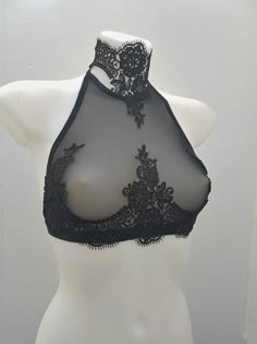 this is a closeup image of a black lace bralette with a halter neckline, it is worn on a white mannequin. the bralette is made of delicate black lace and features intricate embroidery. the fabric is seethrough, revealing the shape of the body underneath. the halter neckline is adorned with a delicate lace trim.