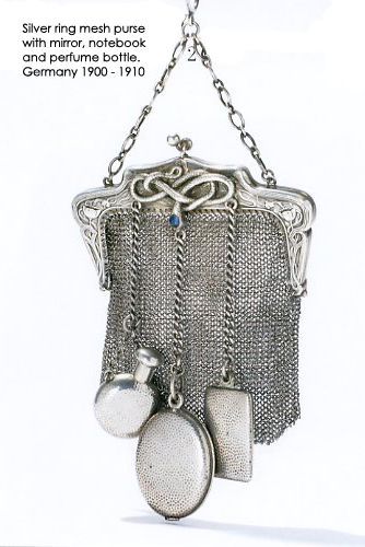 a silver ring mesh purse, with mirror, notebook, and perfume bottle, originating from germany between 19001910. the purse features a chain handle and intricate detailing. it includes a perfume bottle, notebook and mirror, all attached to the purse by chains.