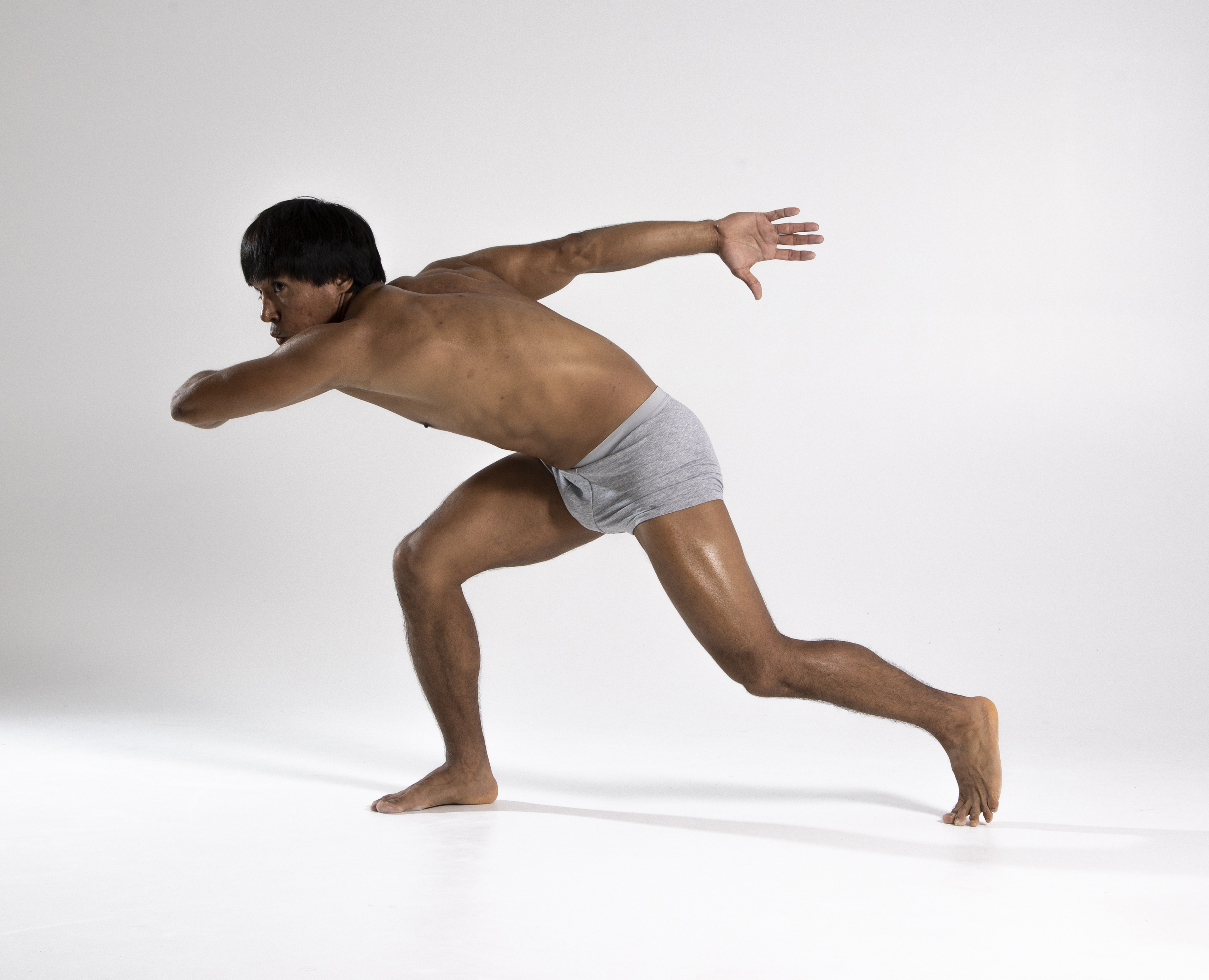 a shirtless man wearing underwear is in a running pose in a studio shot.