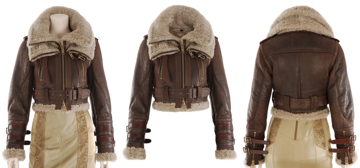 the image shows a brown leather and sheepskin aviator jacket from three different angles: front, back, and side.  the jacket is cropped, has a fur collar, and is belted at the waist.  it features brown leather straps on the cuffs. the jacket is displayed on a mannequin wearing a beige skirt.