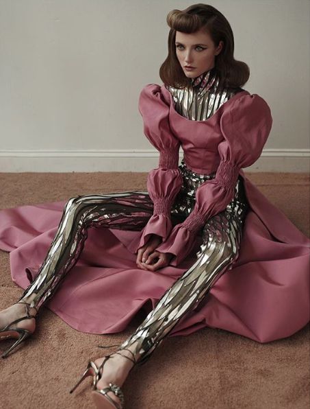a fashionable woman in a pink dress and silver sequin pants poses for a photo shoot in a studio. she has a vintage style and is wearing high heels. she has an elegant and sophisticated look.