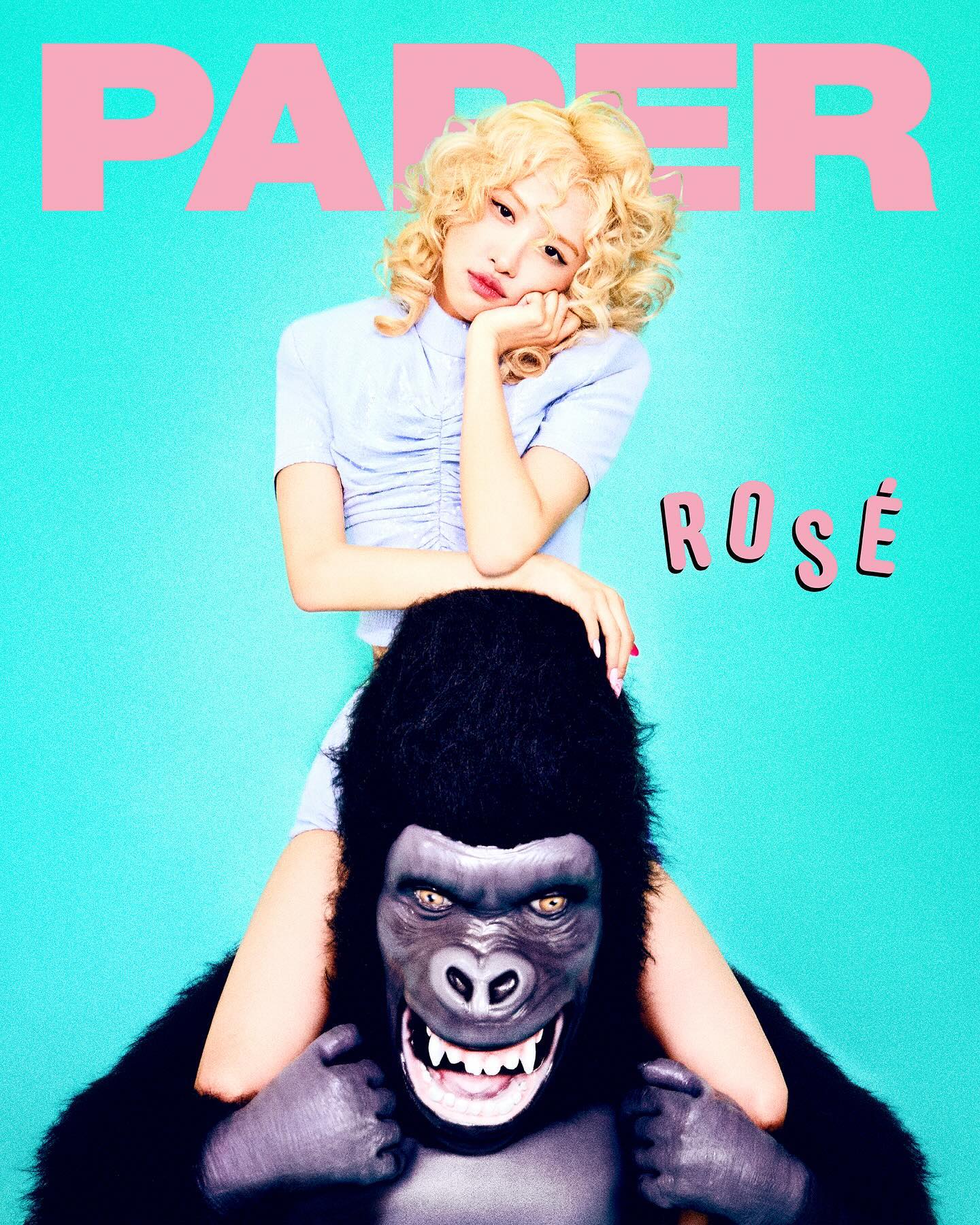 the image is a promotional shot from a photoshoot for paper magazine featuring rosé, a member of the popular south korean girl group blackpink.  rosé is depicted with blonde, curly hair, wearing a light blue, ruffled shortsleeved top and dark bottoms. she playfully sits on a large, realisticlooking gorilla costume. the background is a vibrant teal color. the paper magazine logo is prominently displayed in pink at the top, with rosé's name also written in pink. the overall mood is fun, youthful and stylish, aligning with the aesthetic of paper magazine and rosé's image.