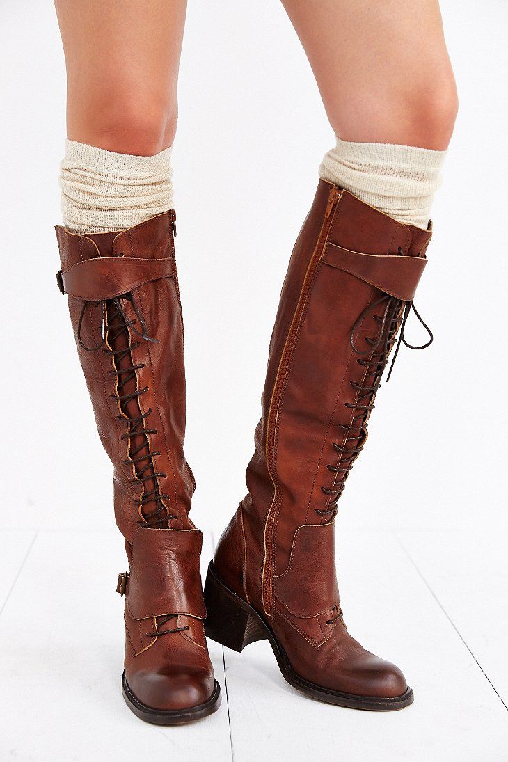 a pair of women's kneehigh brown leather boots with laces up the front.  the boots have a chunky heel and a round toe. they are paired with white socks that peek out at the top of the boots.  the photo is taken on a light wood background.