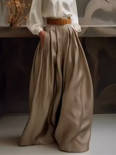 a woman in a white shirt and flowing, pleated brown pants stands elegantly in a studio setting. the fabric has a silky sheen and drapes beautifully, creating a timeless and sophisticated look.  the woman's pose emphasizes the flowing nature of the fabric, making the outfit appear both comfortable and chic.