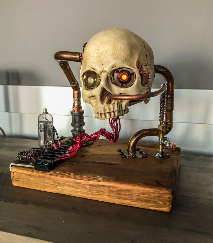 a steampunk skull sculpture with a red glowing eye, copper pipes and a wood base. it looks like an art piece or a lamp. the skull is detailed and has a futuristic, vintage aesthetic. it is a unique and creative piece of art that would make a great addition to any steampunk collection.