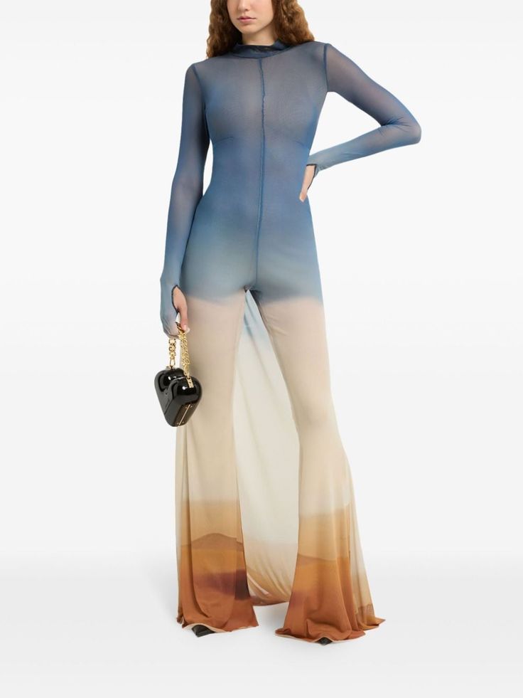 a female model is wearing a blue ombre mesh jumpsuit with long sleeves, standing against a white background. she has black handbag hanging from her arm, the model is wearing a light makeup.