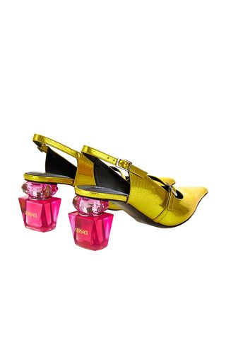 a pair of yellow high heels with a gold finish. the heels are shaped like perfume bottles with a pink base and a pink label that reads "versace". the shoes are a stylish and elegant choice for any occasion.
