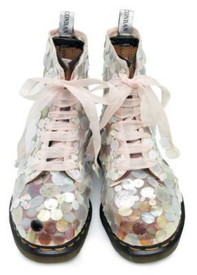a pair of dr. martens boots are heavily embellished with iridescent sequins and pink ribbon laces. the boots are light pink and the sequins are various pastel shades.  the conran label is visible on the tongue of each boot. the image shows the boots from a slightly elevated angle against a white background.