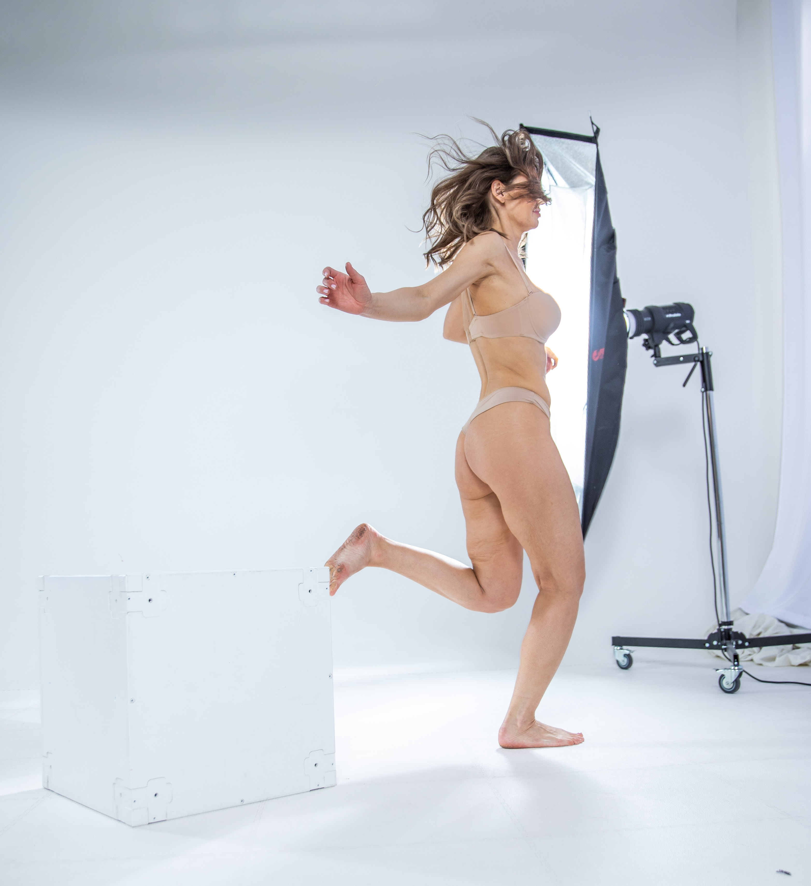 a woman in underwear is captured in a studio setting, with a softbox providing lighting. she is barefoot, and the image emphasizes her beauty.