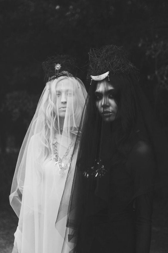 two women stand side by side, their faces partially obscured by veils, with one in a white dress and the other in a black dress. they create a striking juxtaposition of light and dark. the white veil creates a ghostly and ethereal effect, while the black veil adds a sense of mystery and intrigue. their headwear and attire convey a sense of gothic, magical, and captivating allure. the image has a dark and mystical feel, suggesting a hidden world or story.