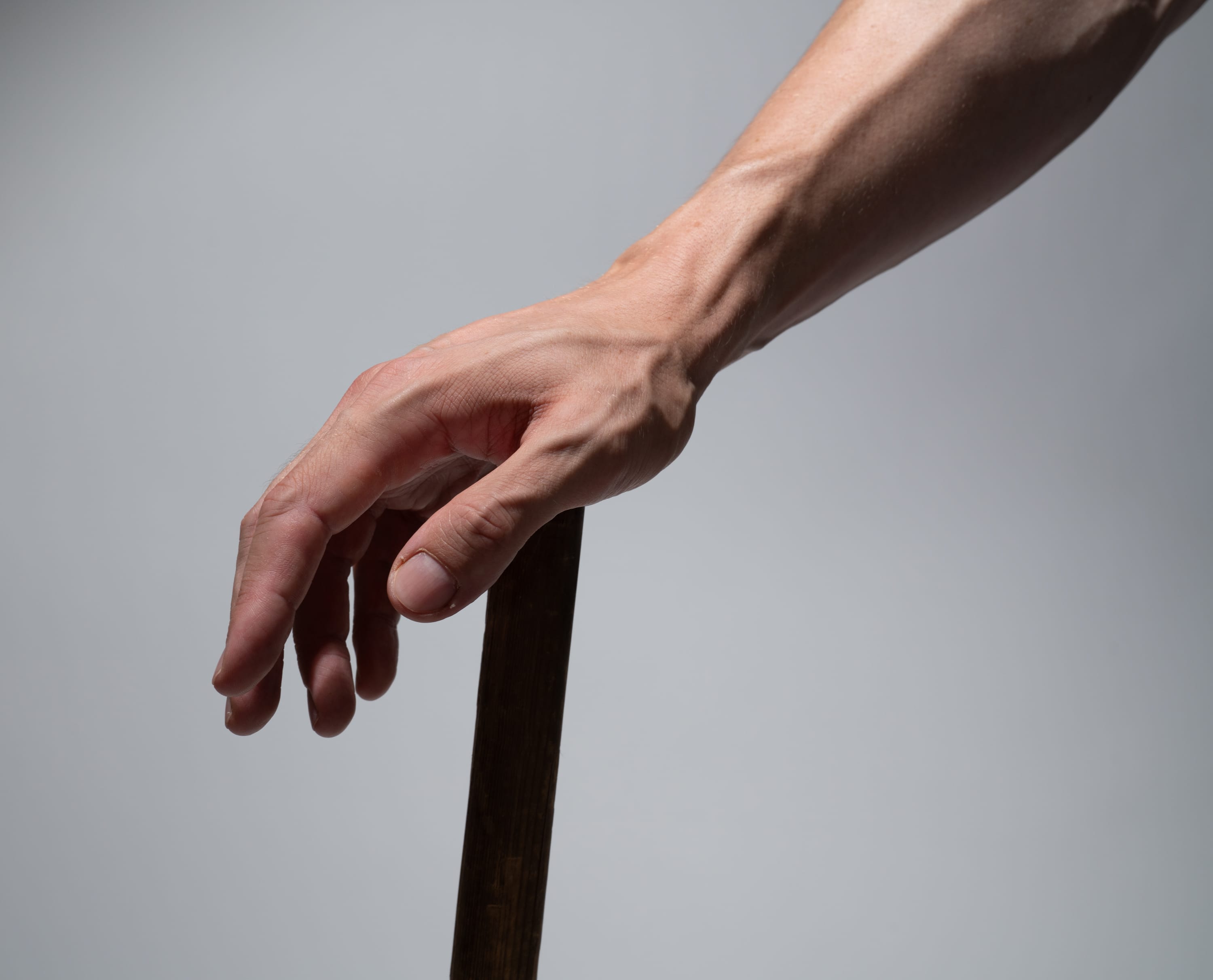 the image shows a closeup view of a man's hand gripping a dark brown walking stick against a neutral gray background. the hand is welldefined, showcasing prominent veins and highlighting the strength and support it provides. the soft lighting emphasizes the texture of the skin and the wooden surface of the walking stick.