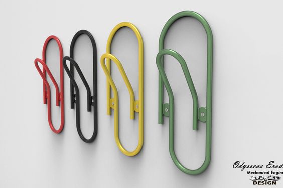 this is a modern coat rack design. it is made of metal and looks like a paperclip. it comes in four colors: green, yellow, red, and black. it is mounted on a white wall and is a great addition to any modern home.
